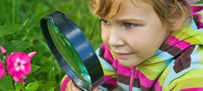 Child looking at a flower through a magnifying glass